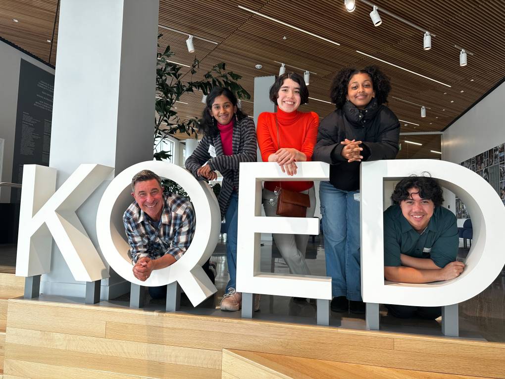 KQED's Scott Shafer poses with members of the Youth Advisory Board in front of the KQED logo