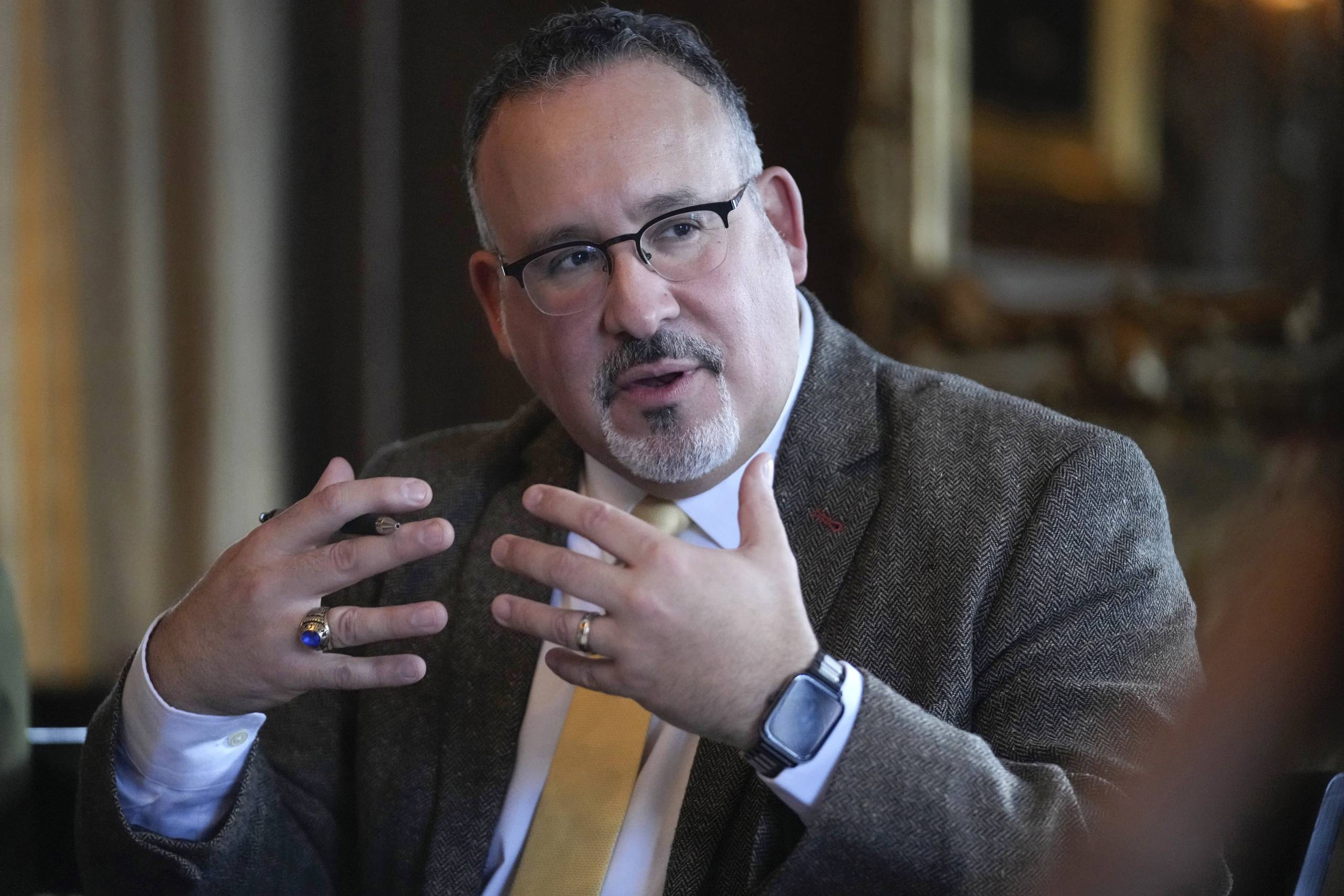 A white man wearing glasses and a business suit expresses himself with his hands.