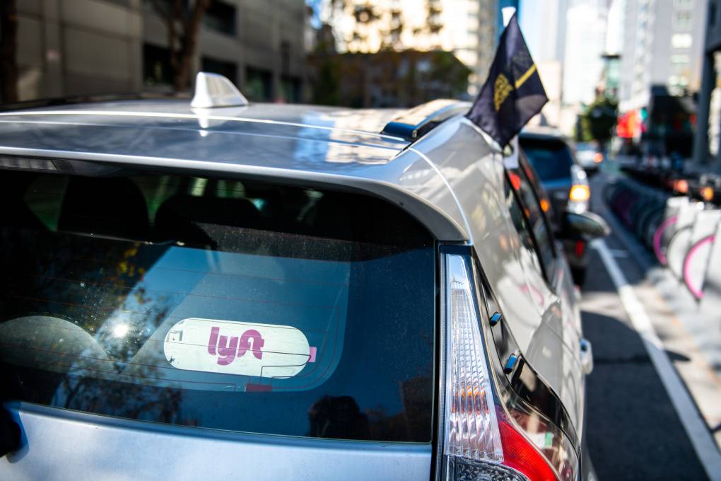 A car with a Lyft sign drives with a black flag in the window.