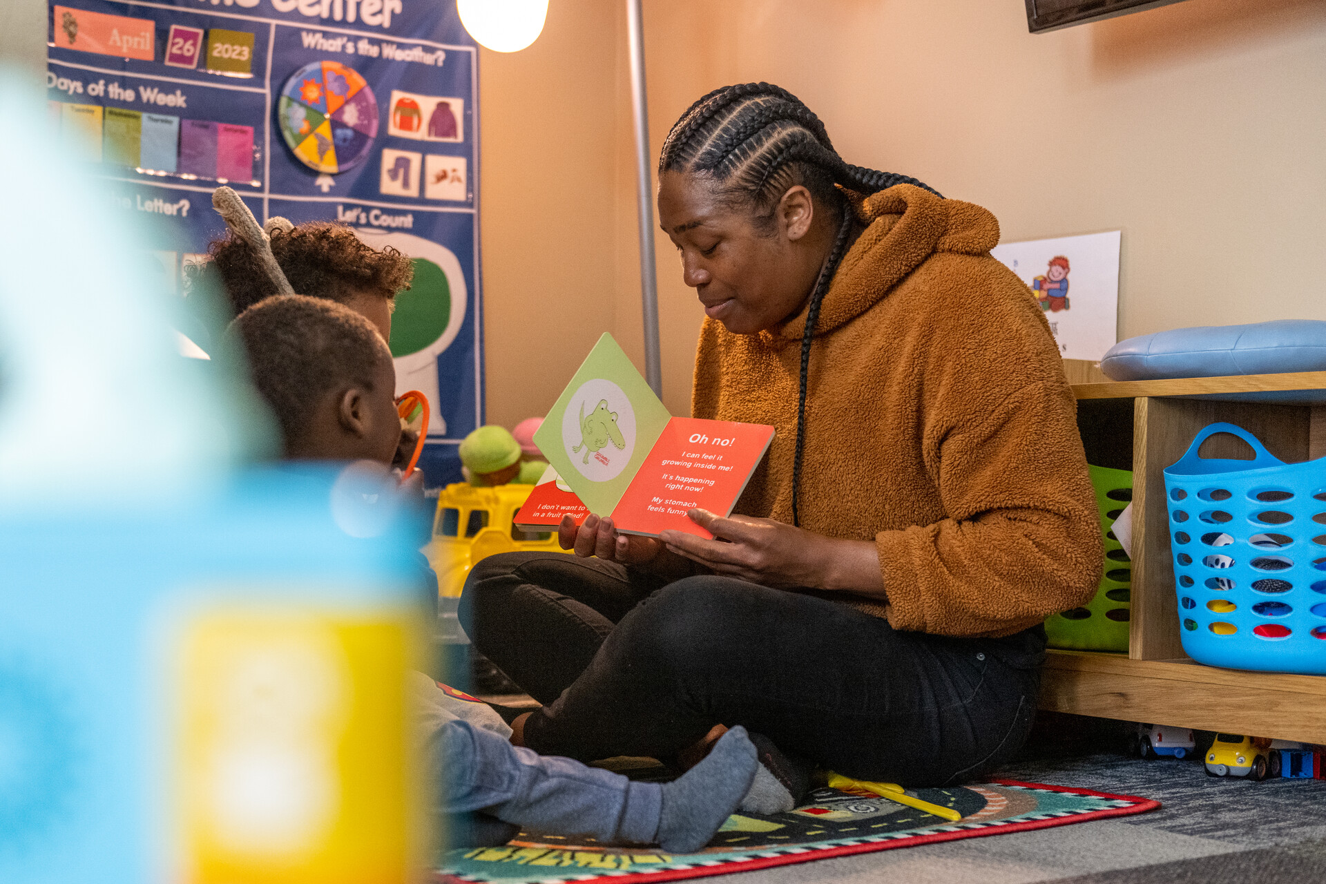 A woman is sitting on the floor showing an open book to a child.