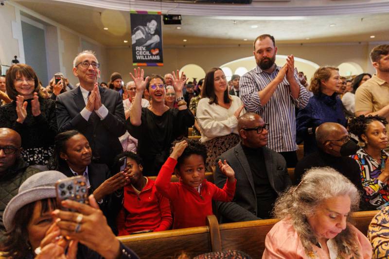 Several people stand clapping in a church.