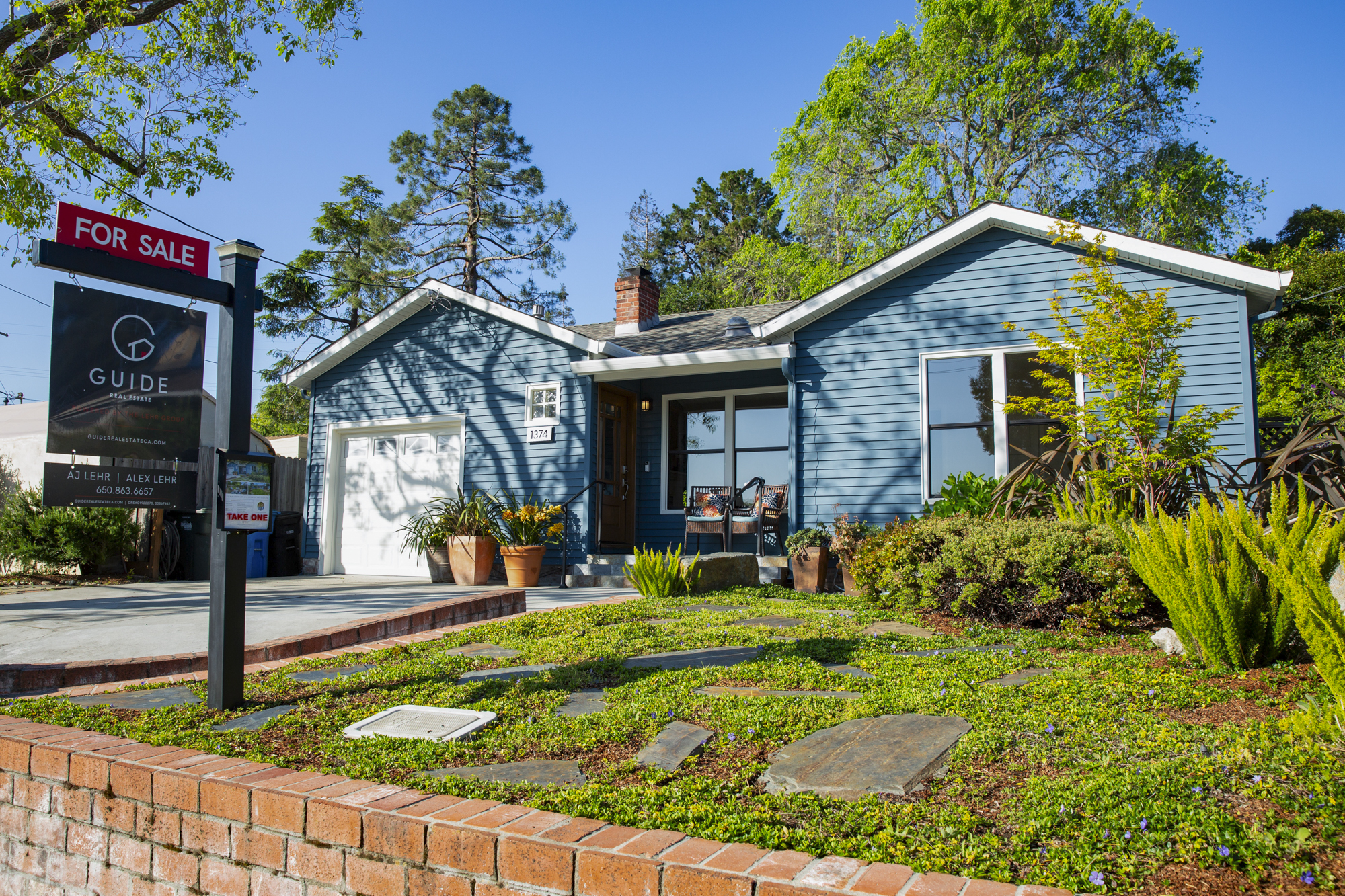 A blue, one-story home with a 'For Sale' sign in the front yard.