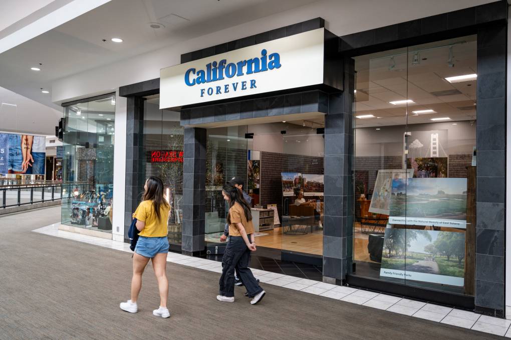Two people walk past a sign that says 'California Forever.'