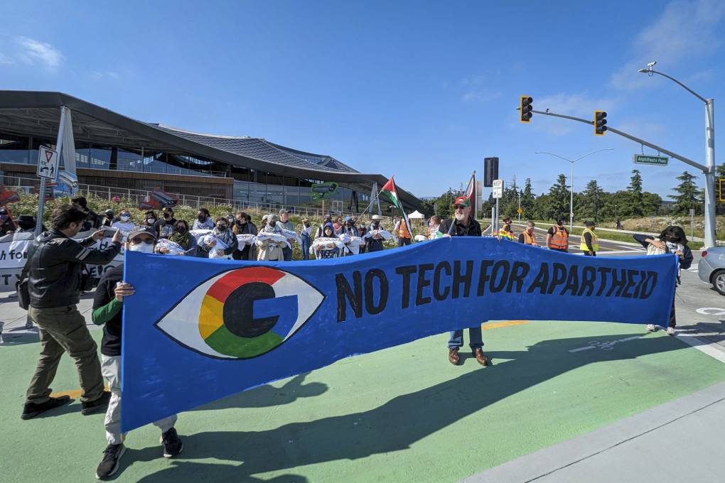 Several people hold up a blue banner with a Google icon over an eye that reads "No Tech for Apartheid."