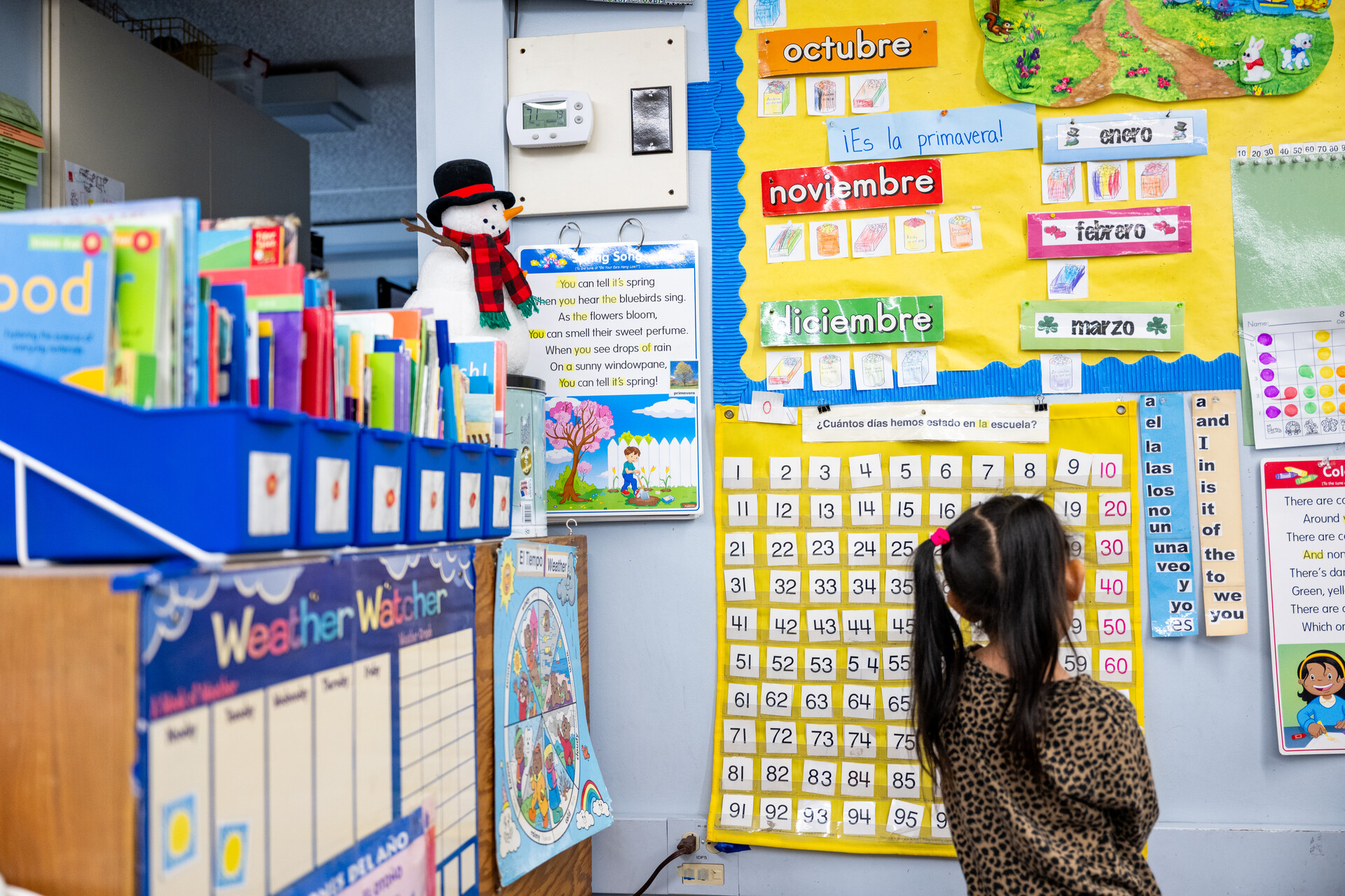 A young girl looks at a bilingual calendar on a classroom wall