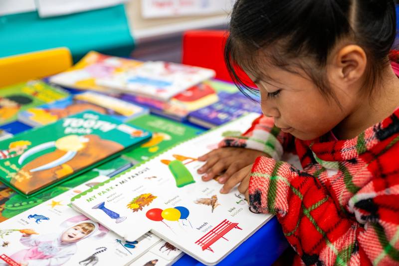 A young girl reads a bilingual exercise book at a classroom table