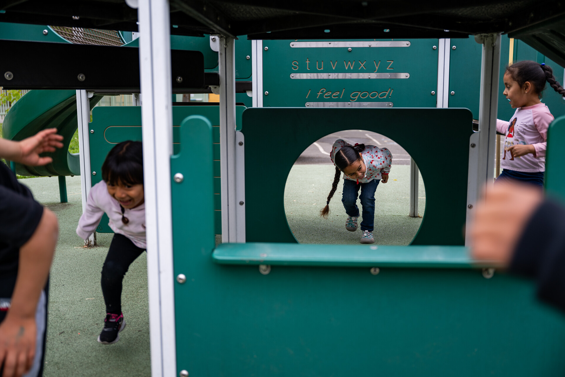 A young girl is seen through a circular opening in an outdoor play gym structure