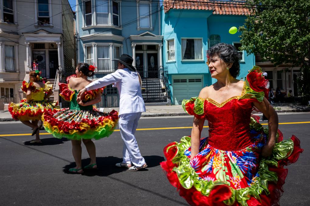 A man and woman dance in white clothing and colorful dresses in the street.