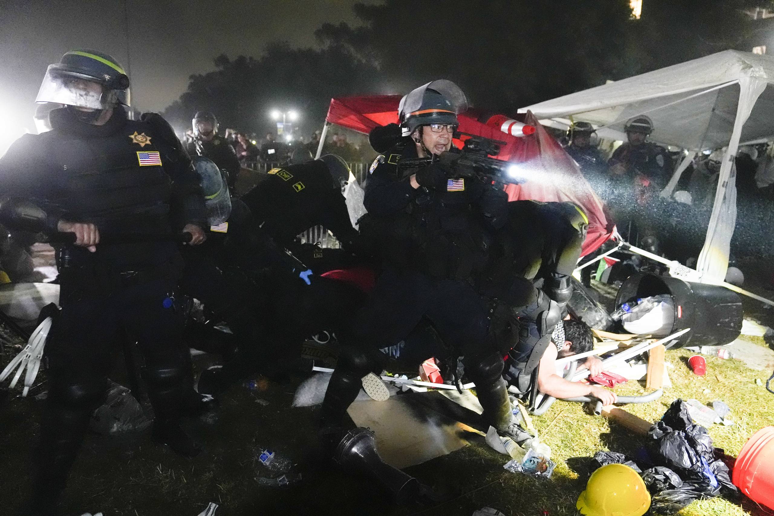 Multiple police knock over a barricade and point their weapons.