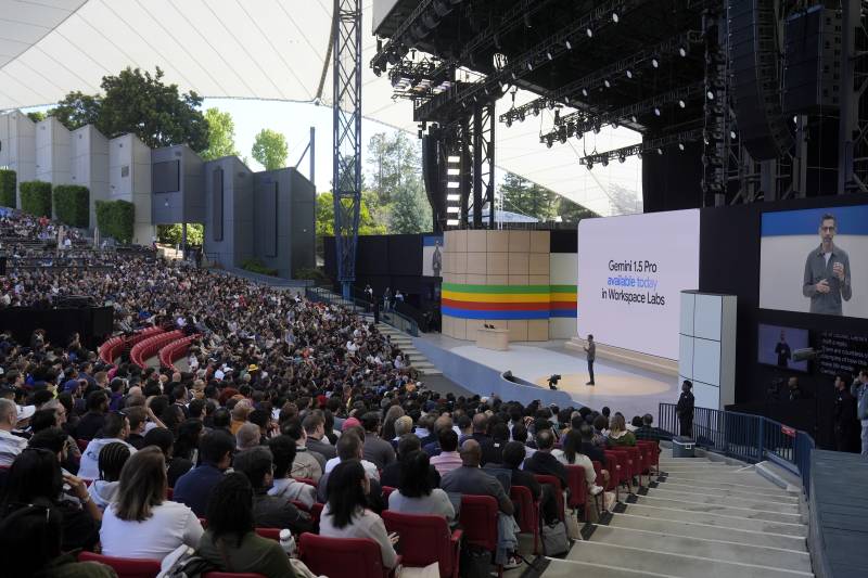 Hundreds of people sit at an amphitheater, looking at one person on stage.