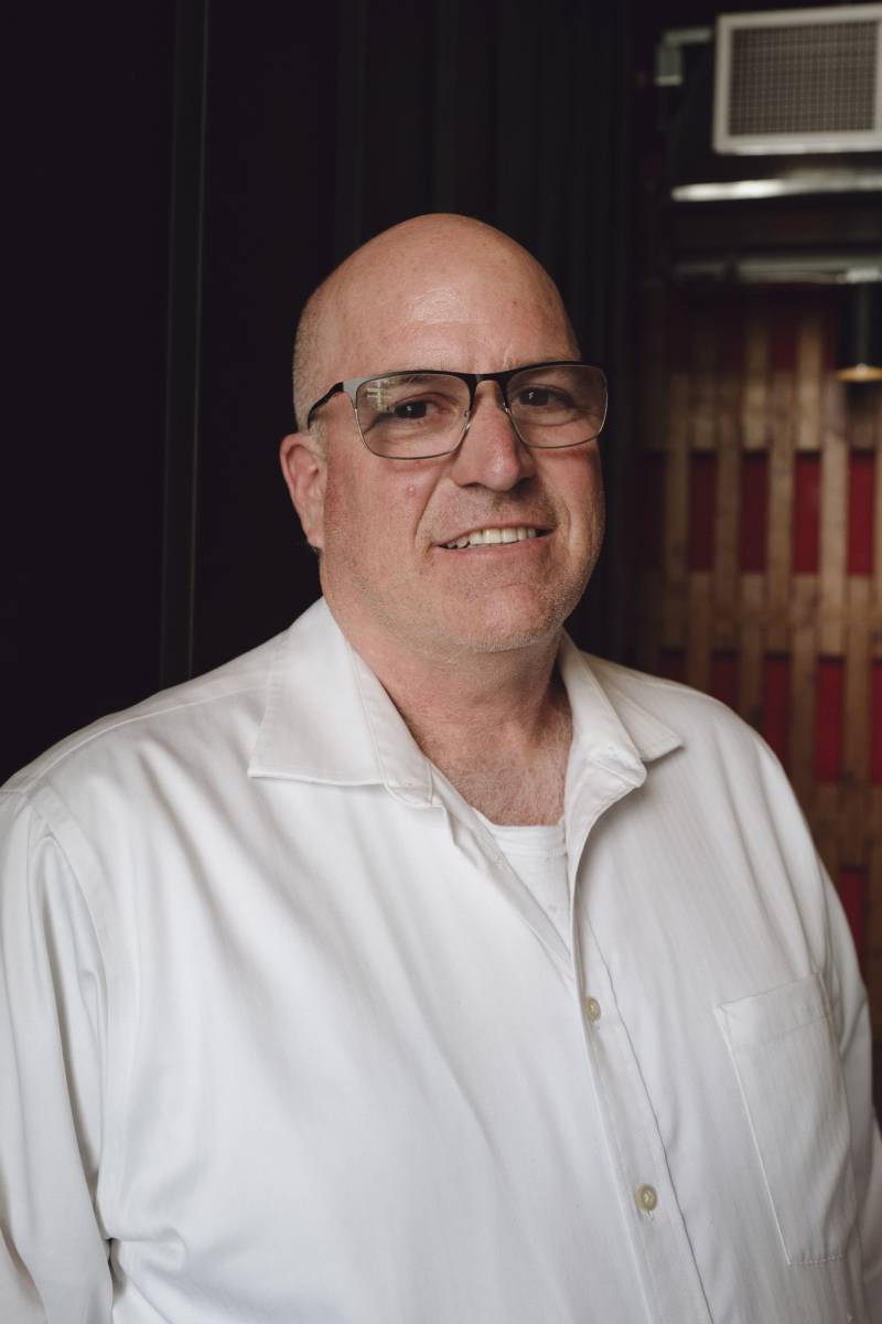 A headshot of a white man wearing glasses and a white shirt.