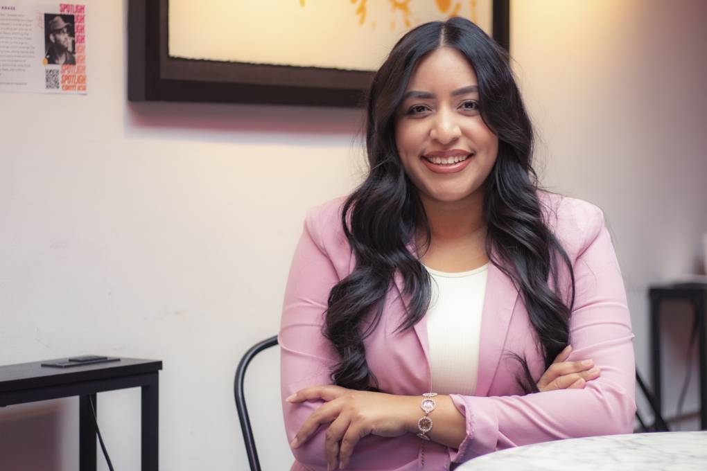 A Latina woman wearing a pink blazer seated with her arms crossed.