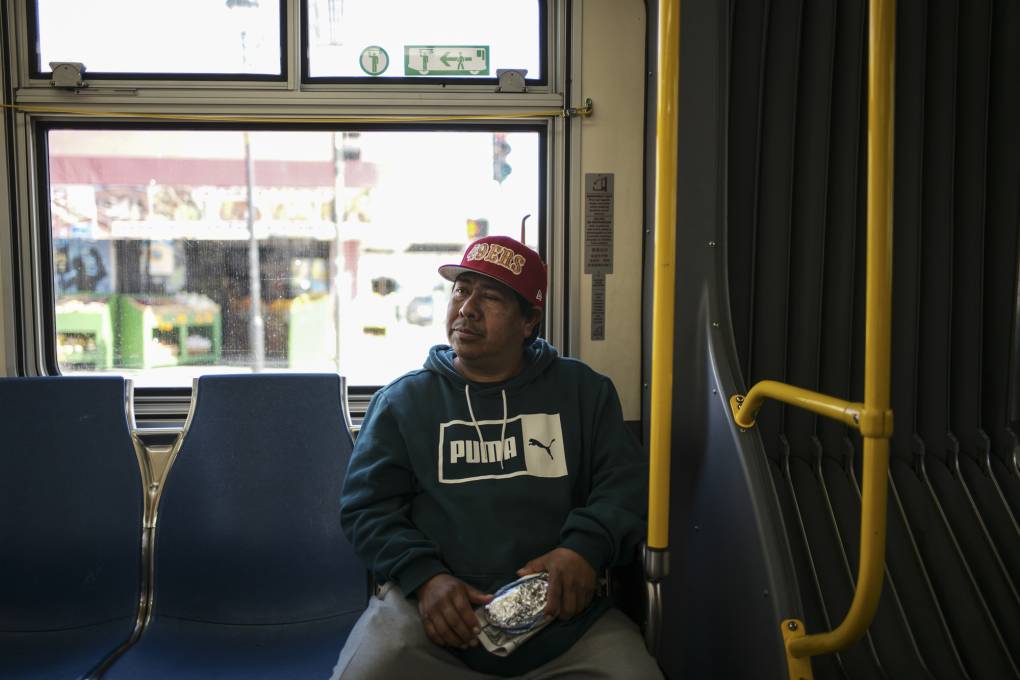 A middle-aged Latino man with a hat sits on a bus.