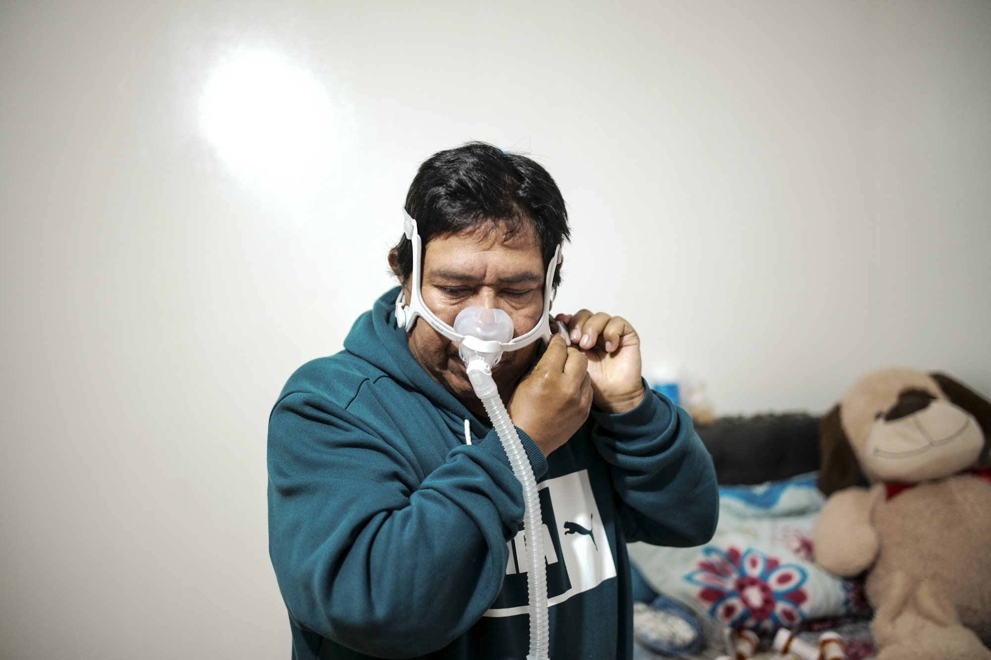 A middle-aged Latino man puts on an oxygen mask at home.