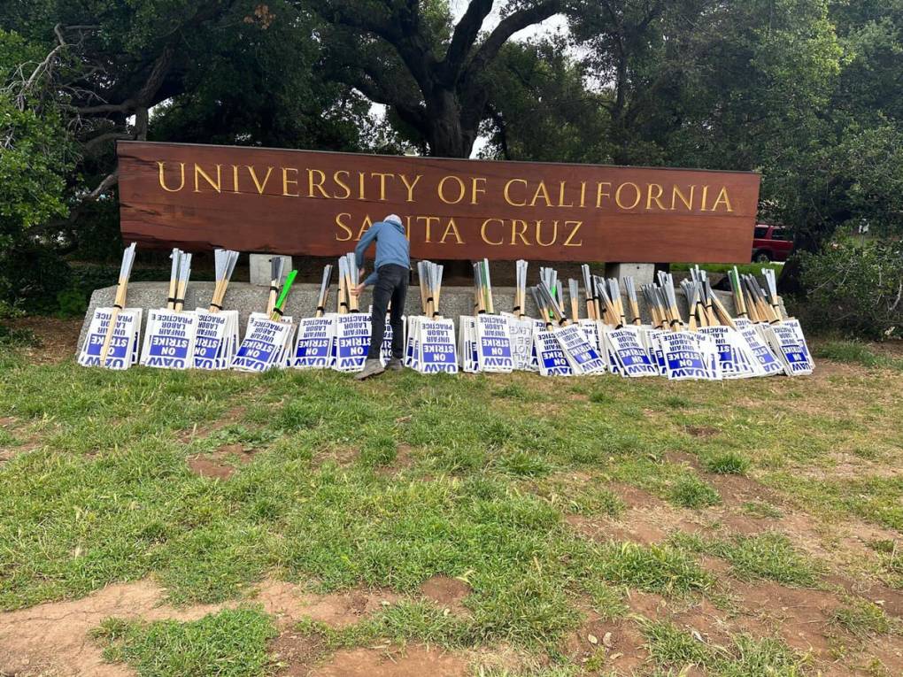 strike signs leaned against a large sign saying "University of California, Santa Cruz"