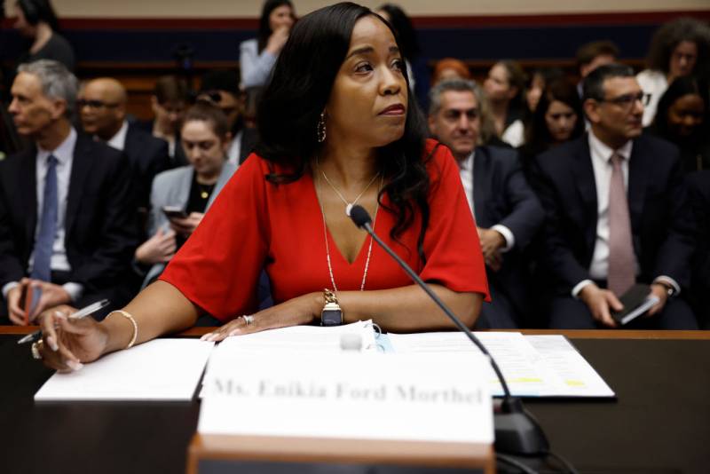 A Black woman in a red dress sits in front of a microphone.