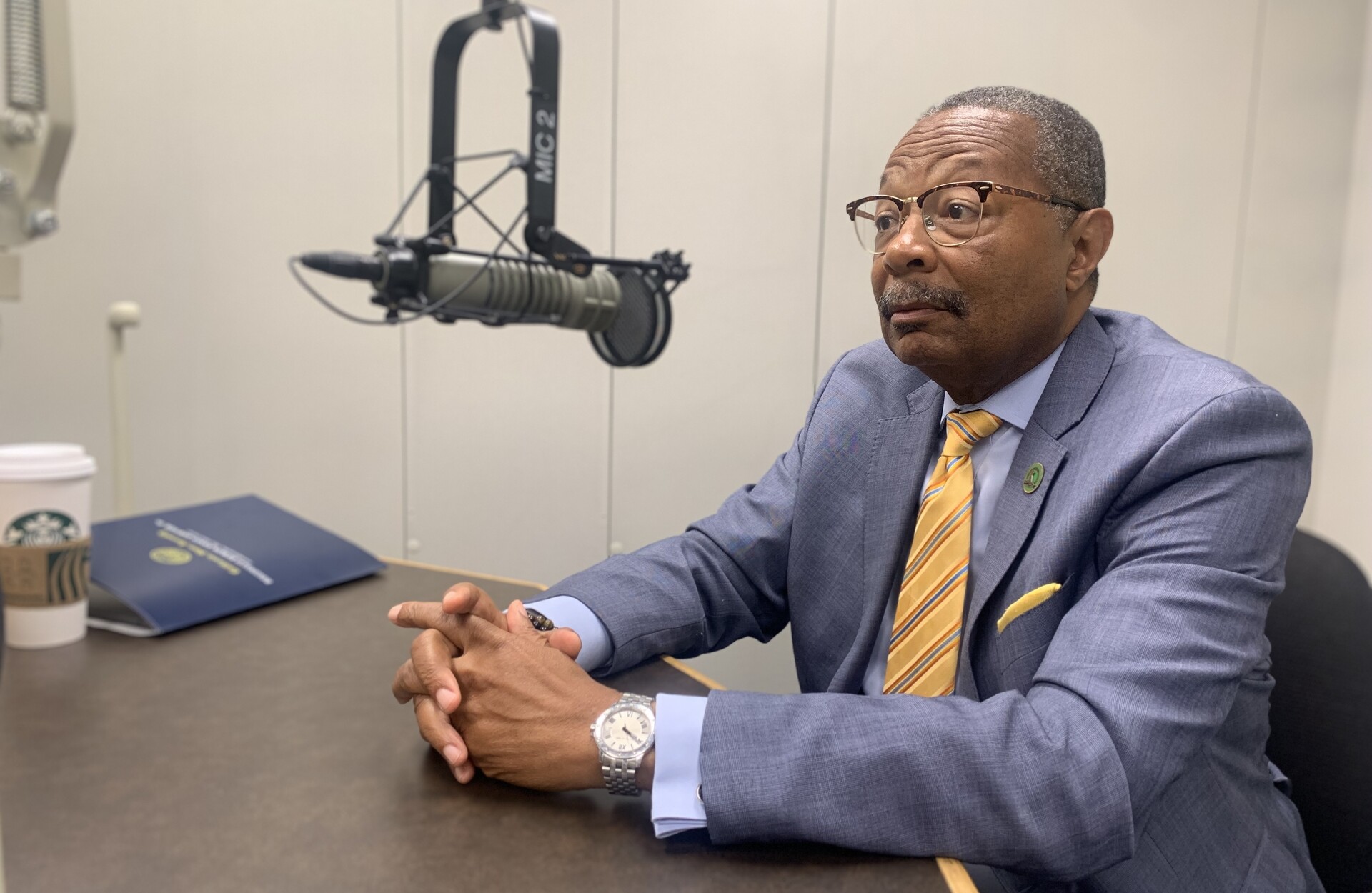 A man in a suite sits next to a microphone.