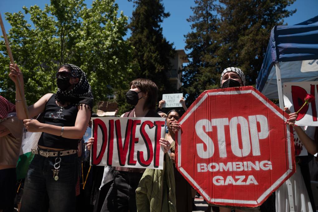 Two college-age students hold up signs that say 'Divest' and 'stop bombing Gaza.'