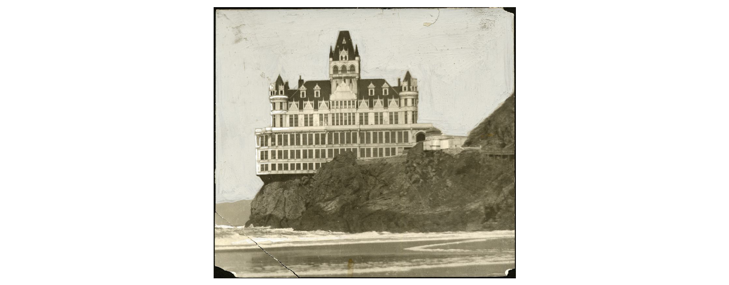 Black and white photo of a massive Victorian-era structure perched on a cliff overlooking the ocean.