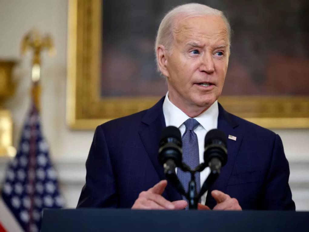 President Joe Biden delivers remarks at a lectern with a microphone, and an American flag in the background.