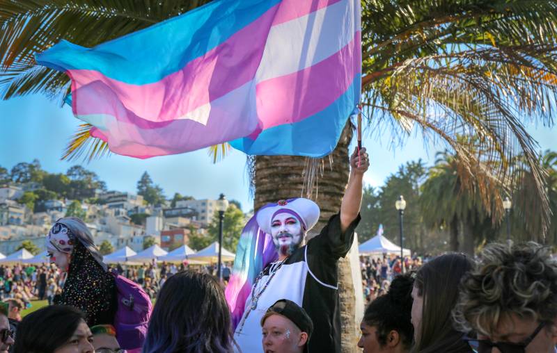 A person waves a pink, blue and white transgender flag among a crowd of people in San Francisco.