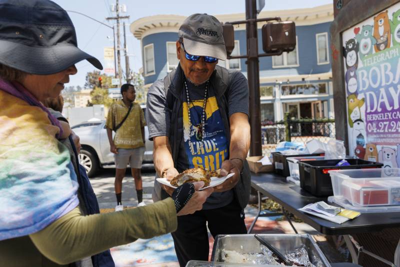 A woman serves a man food on a street.