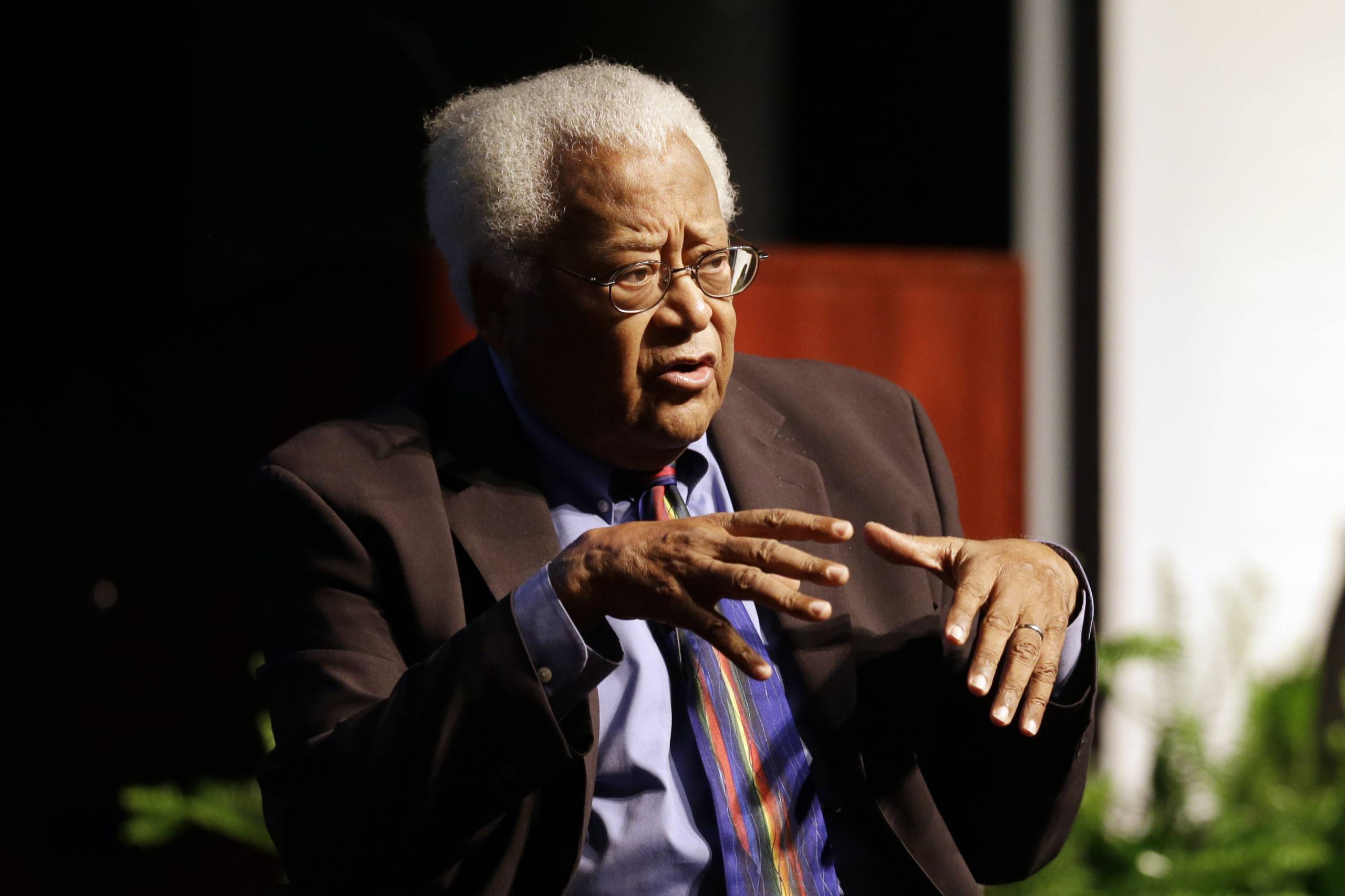 An elderly Black man with glasses speaks while moving his hands.