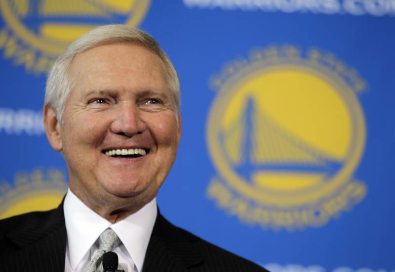 A headshot of a white man wearing a business suit with the Golden State Warriors logo in the background.