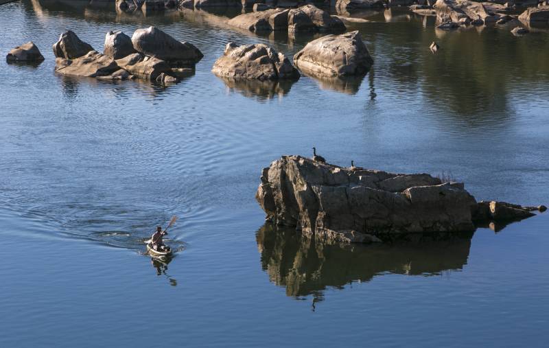 A river filled with large rocks with birds perched on them along with a person paddling in a boat.
