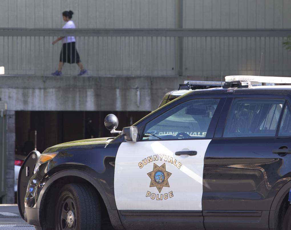 A police vehicle that says "Sunnyvale" on the side is parked while a woman walks in the background.