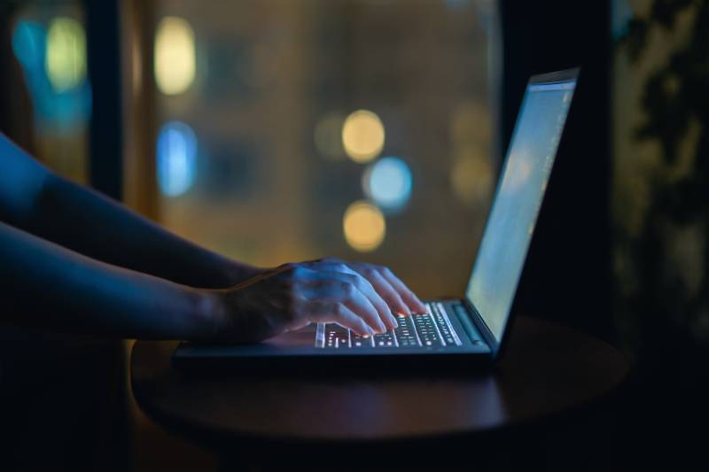 A cropped shot of a woman's hand typing on computer keyboard in the dark.