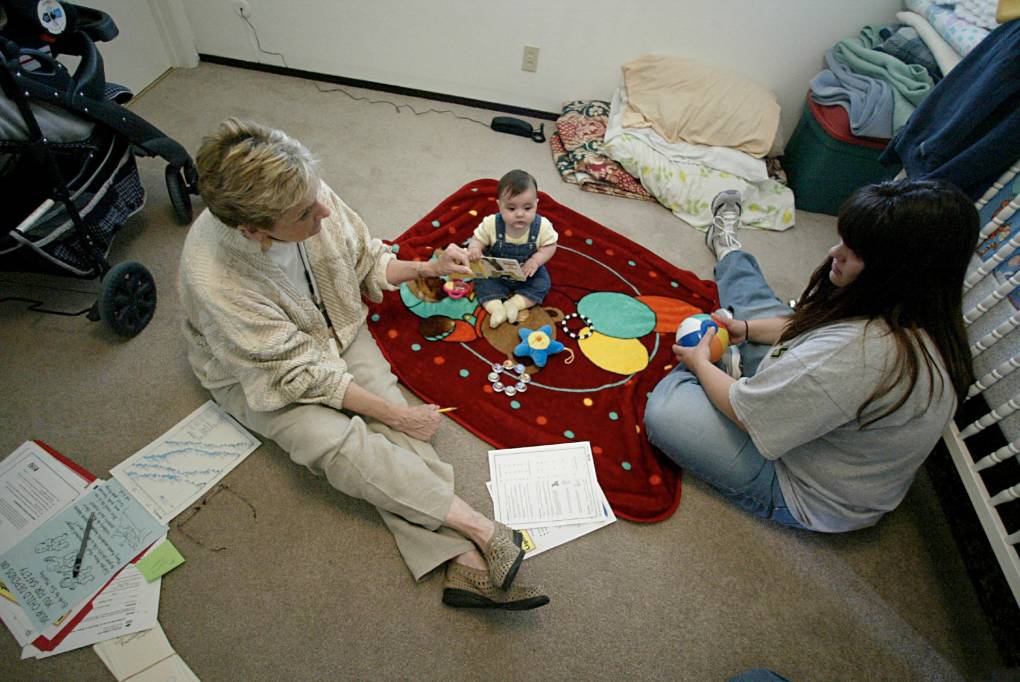 Two women sit on the floor while a baby sits between them.