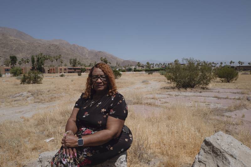 An older Black woman sits in an empty field.