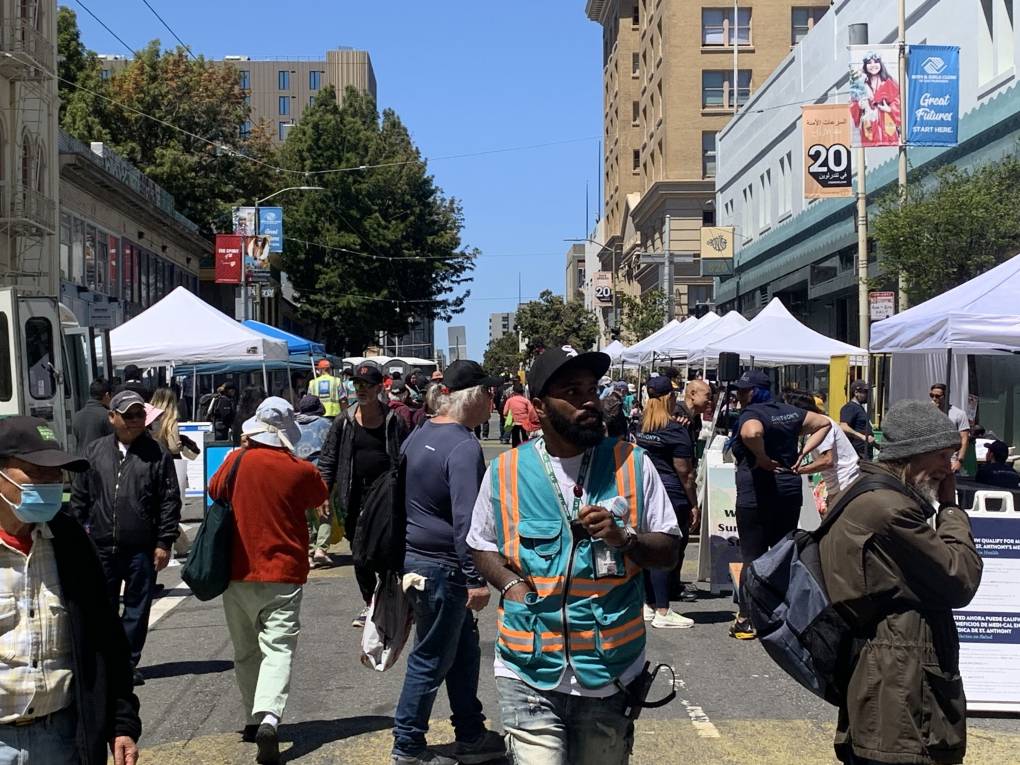 People walking on a street that's been closed off to host an event with many white vendor tents lining either side of the street.