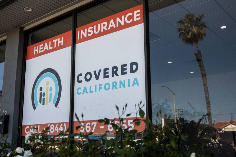 A window has a sign that reads "Health Insurance Covered California."