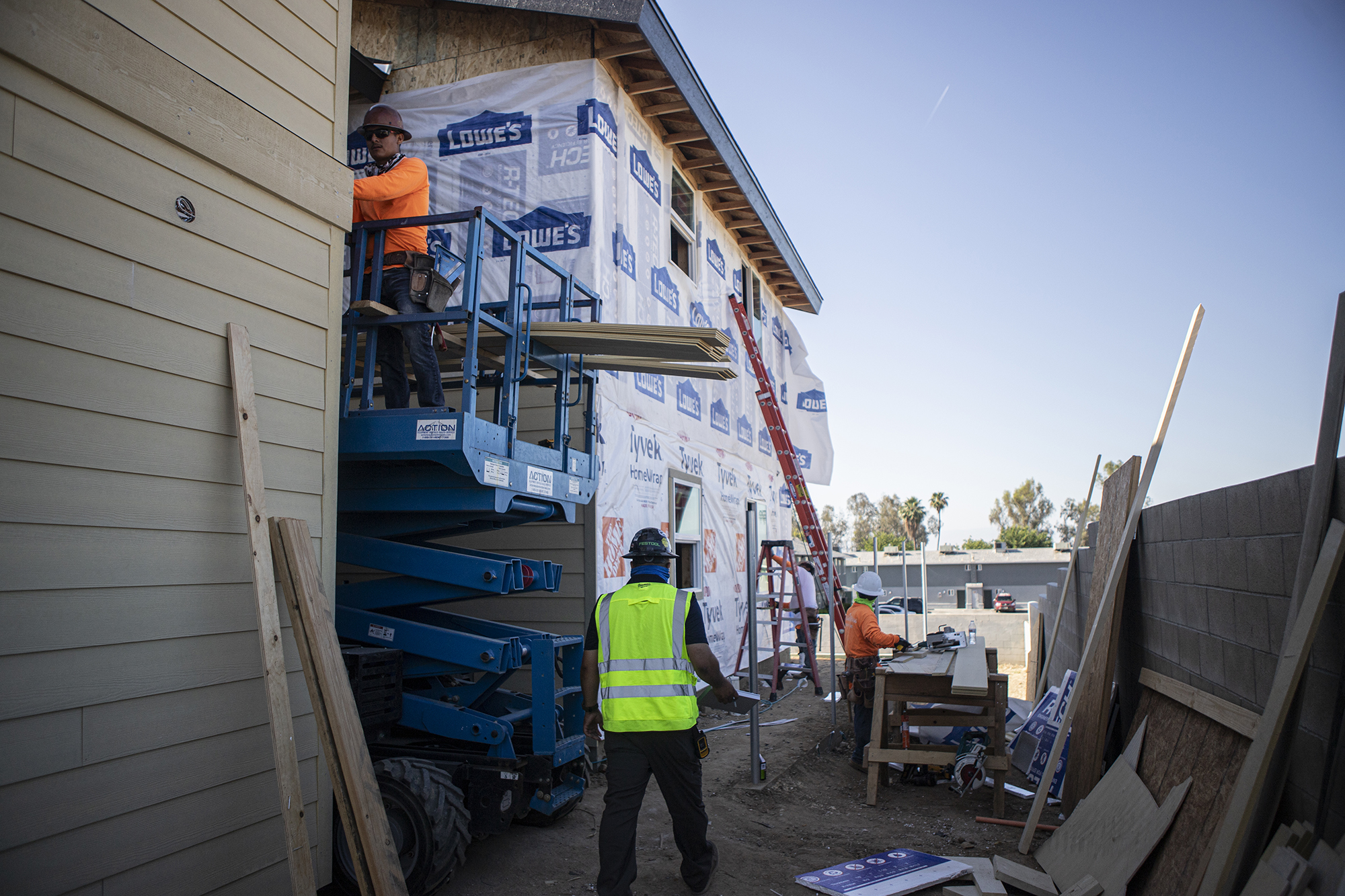 Men wearing bright safety uniforms and hard hats walk around a construction site.