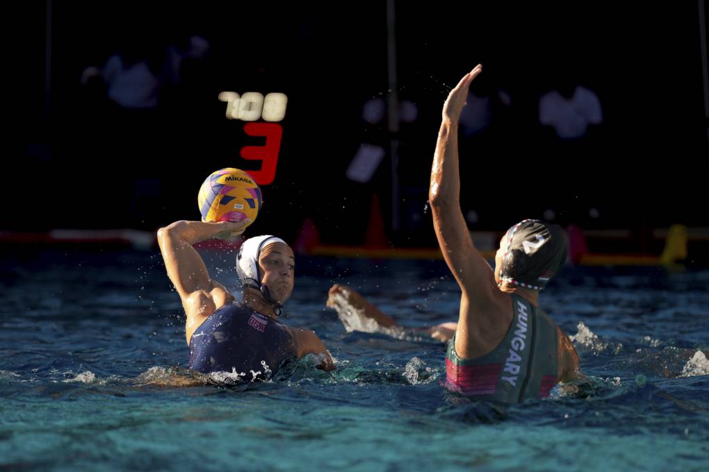 Two women wearing swimming attire play water polo in a pool.