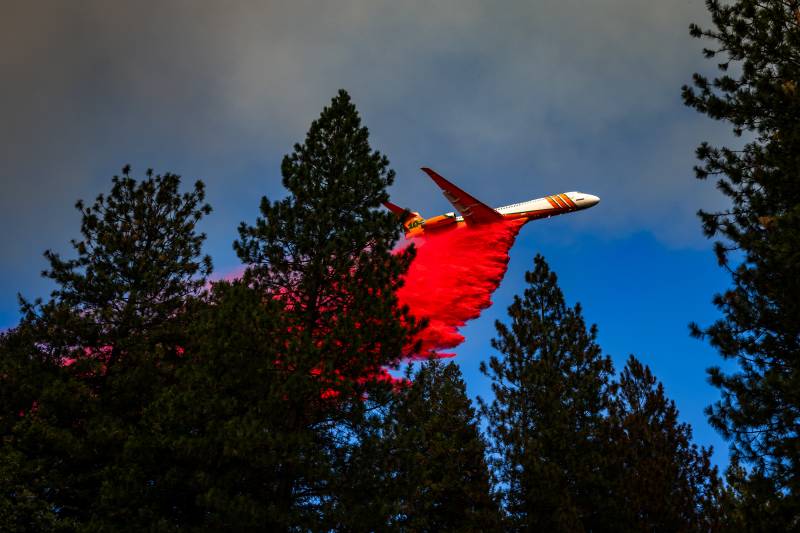Airplane dropping red substance with blue sky in the background.