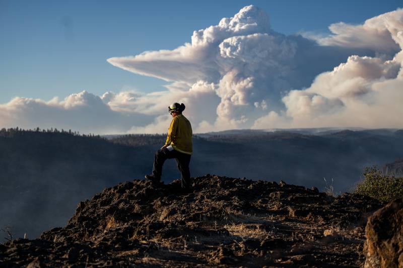 A firefighter in the foreground and a plume of smoke in the background.
