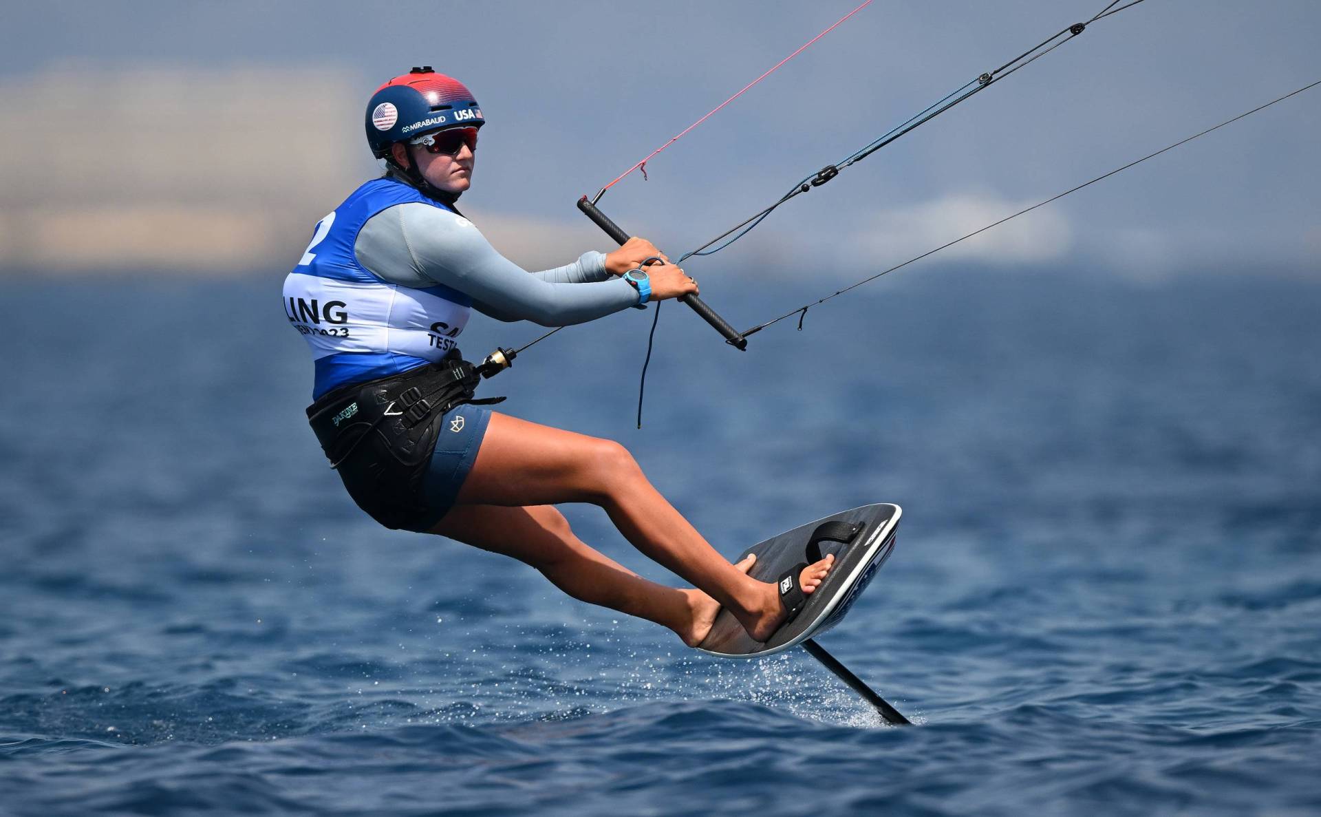 A tanned woman kite boarding in open water.