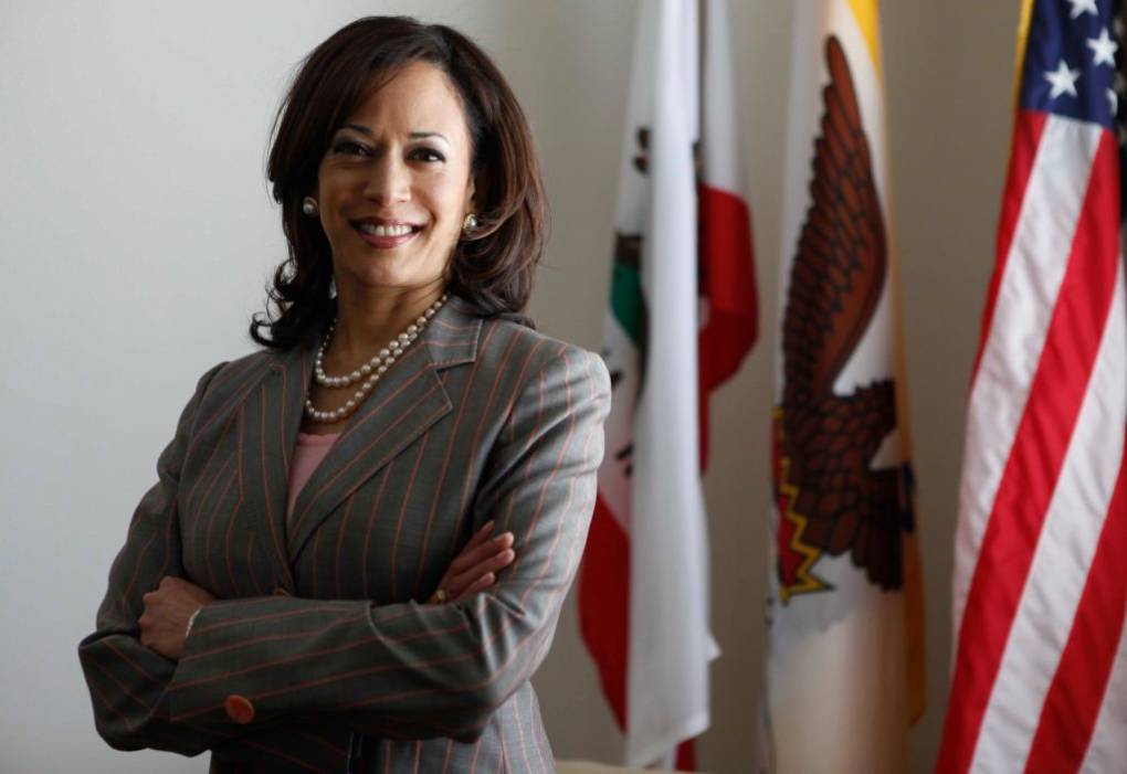 A woman wearing a business suit with two flags in the background.