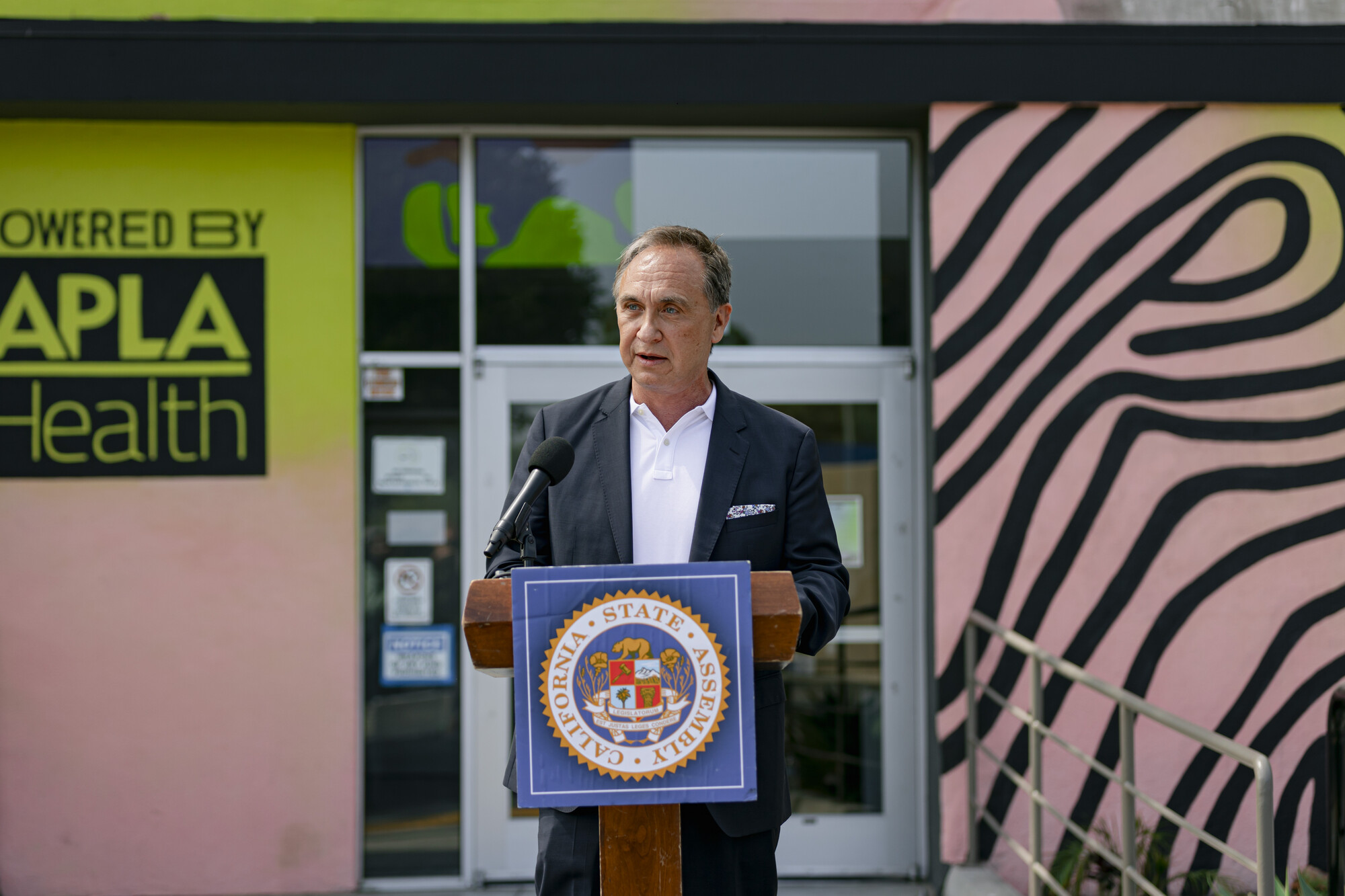 A man stands at a podium speaking at a microphone in front of a glass door.