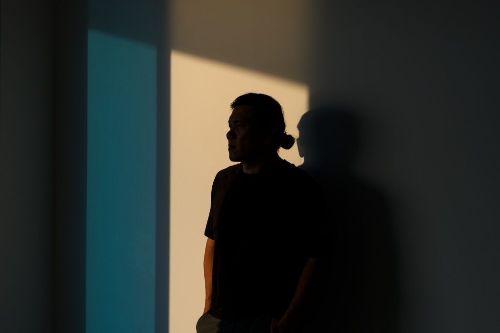A person stands against a wall in shadow, their face obscured.