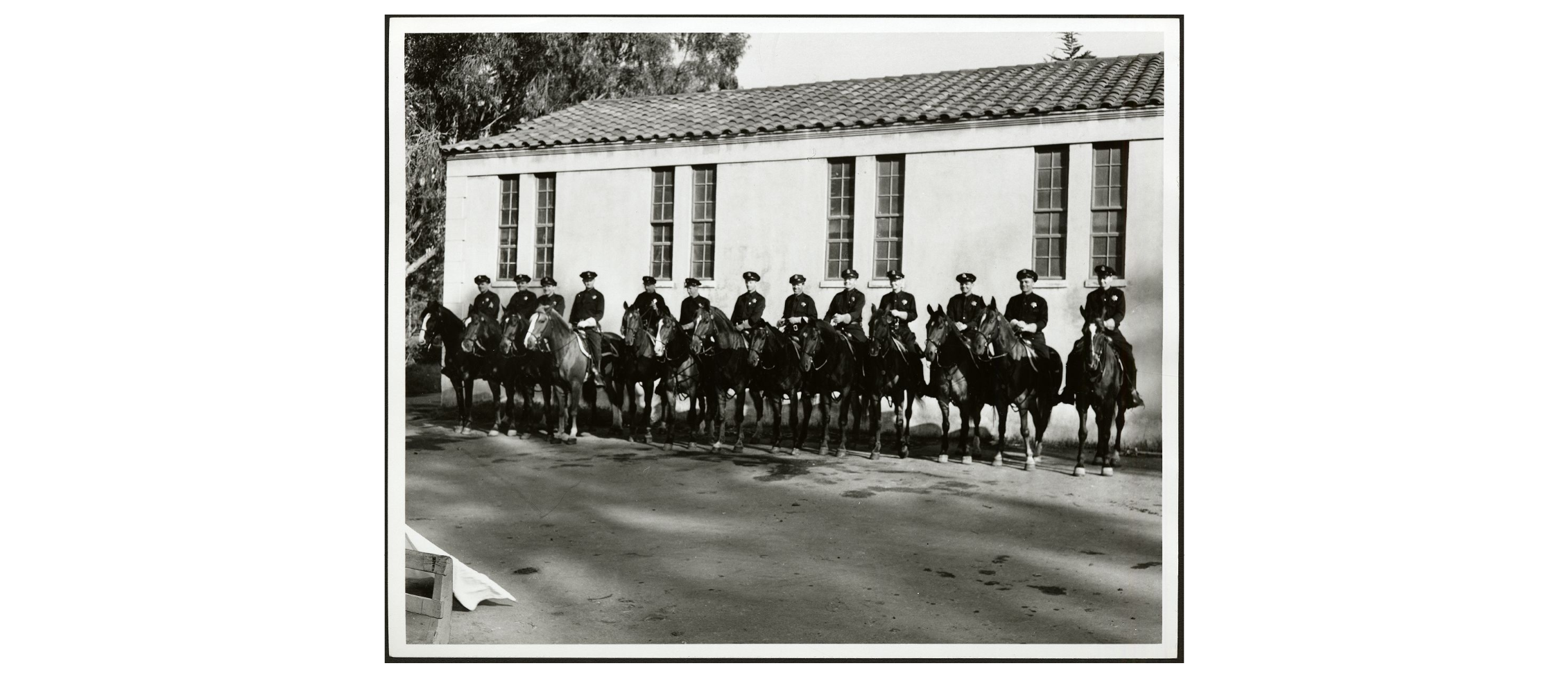 Black and white posed photo of mounted unit in front of the stables in Golden Gate Park.