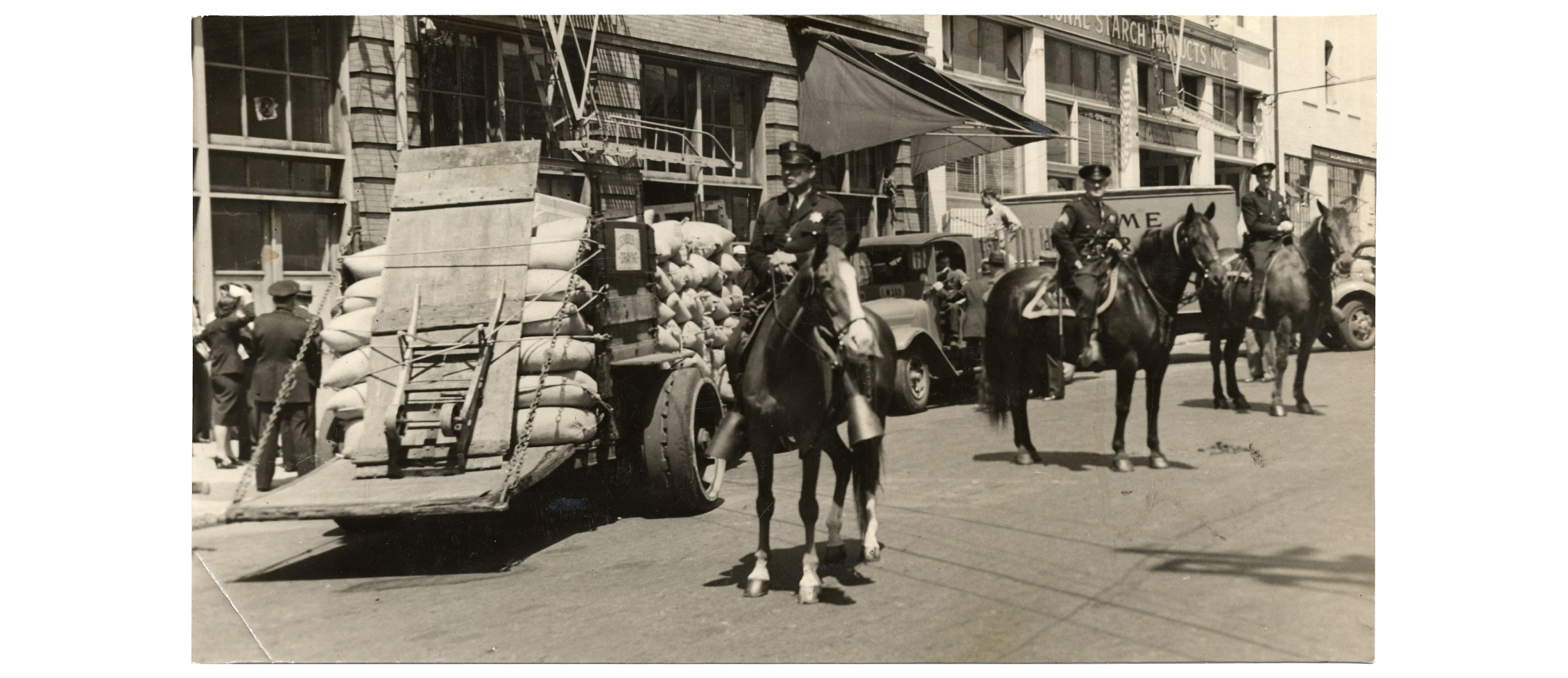 Black and white photo of police on horseback guarding a loaded truck.