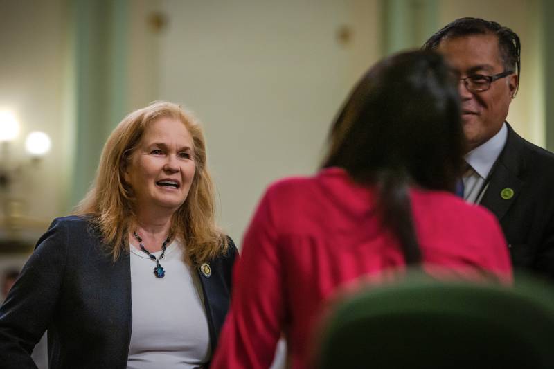 A white woman wearing a black jacket and grey shirt looks at a woman wearing a red jacket that has her back turned to the camera.