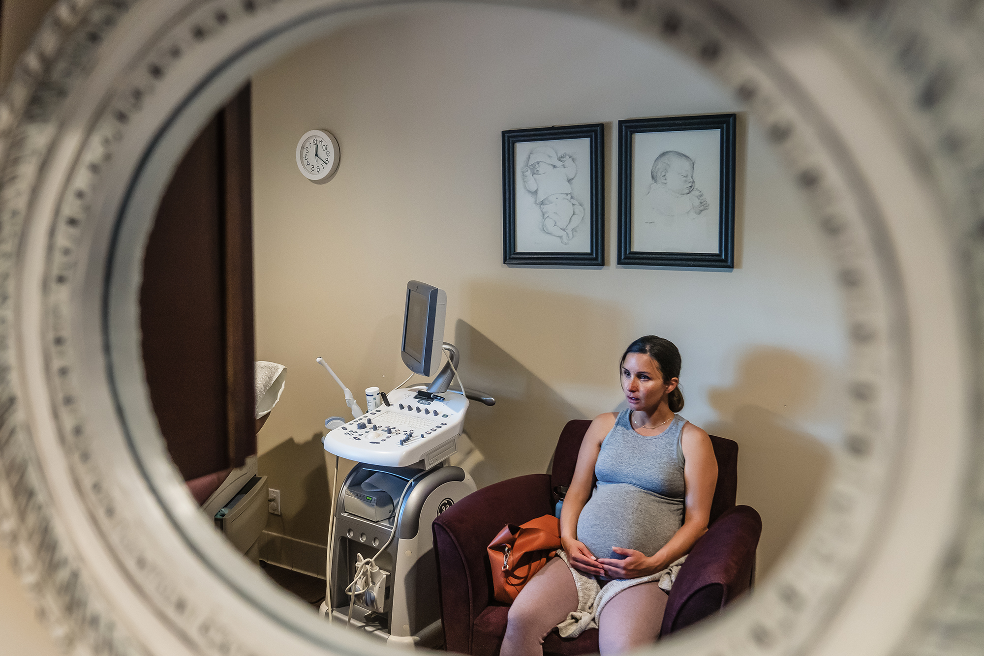 A pregnant woman sits in a room with two framed drawings of babies.