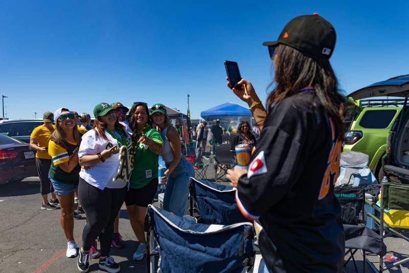 A person takes a photograph of two people posing at a baseball game. 