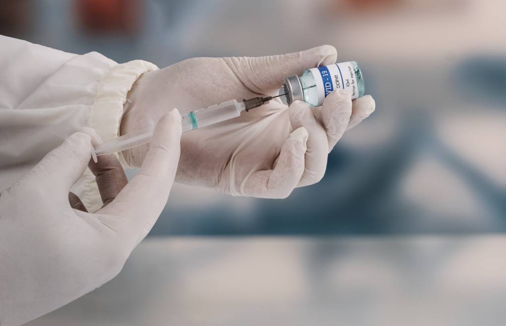 A young doctor in a white protective glove holds a medical syringe and vial.