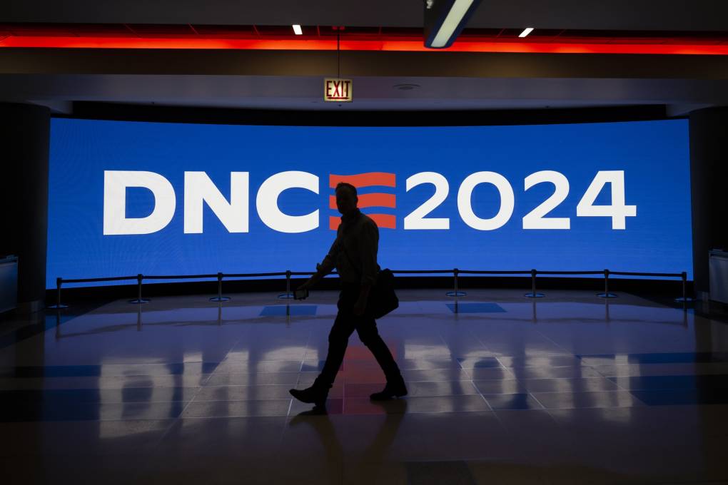 A person walks in front of a digital sign with the DNC 2024 logo